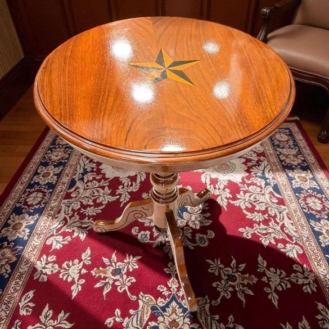 Velador de madera con patas trípode y estrella incrustada, diseño artesanal sobre alfombra clásica en ambiente elegante.