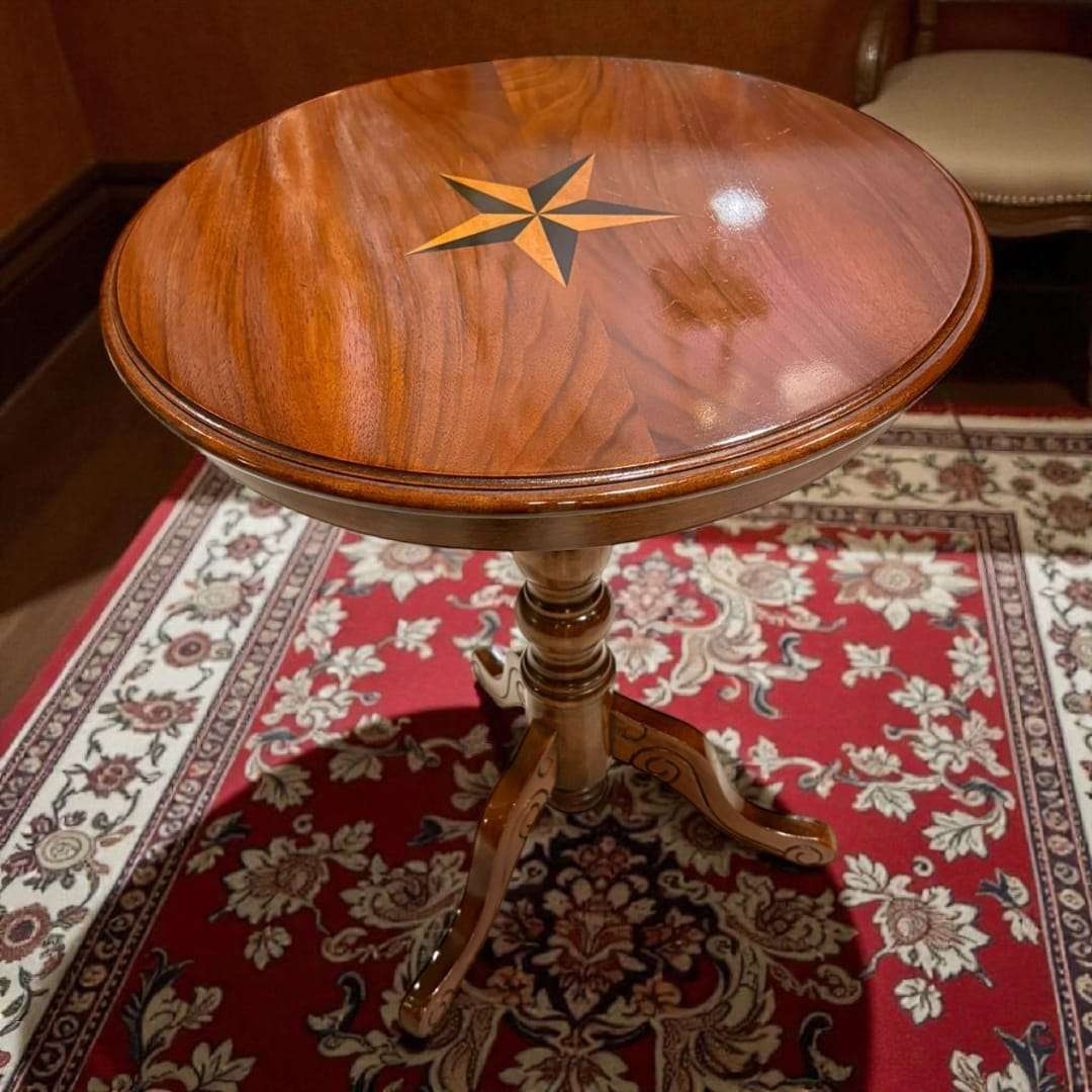 Velador de madera con patas trípode y estrella incrustada, diseño artesanal sobre alfombra clásica en ambiente elegante.