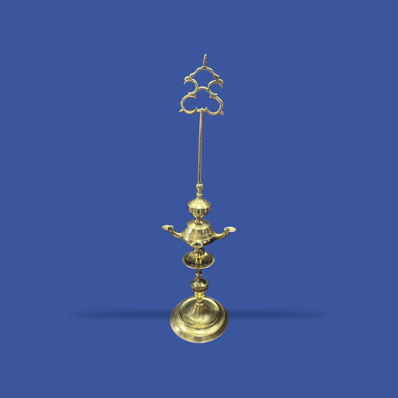 Velón de metal dorado con estructura alta y decorativa, ideal para decoración clásica en interiores solemnes. Diseño vertical con base amplia y detalles ornamentales.