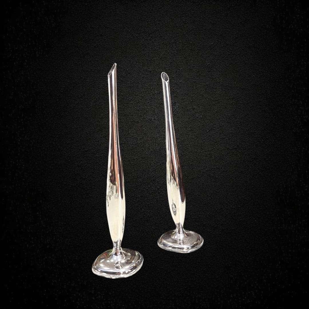 Pareja de violeteros de metal plateado brillando sobre fondo oscuro.