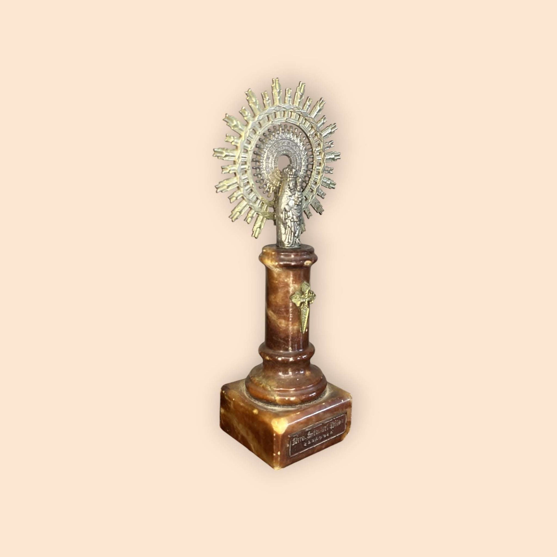 Escultura de la Virgen del Pilar con halo dorado y pedestal rojizo.