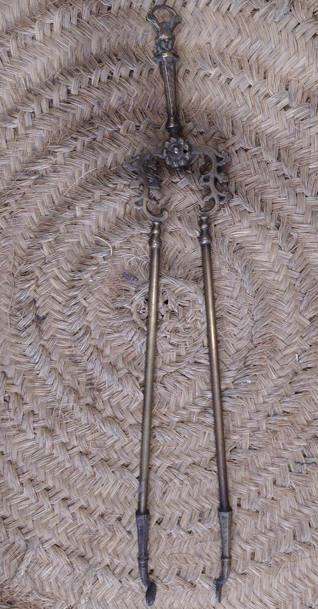 Pinza de chimenea en bronce con diseño ornamental antiguo sobre fondo de mimbre. Decoración elegante para interiores clásicos.