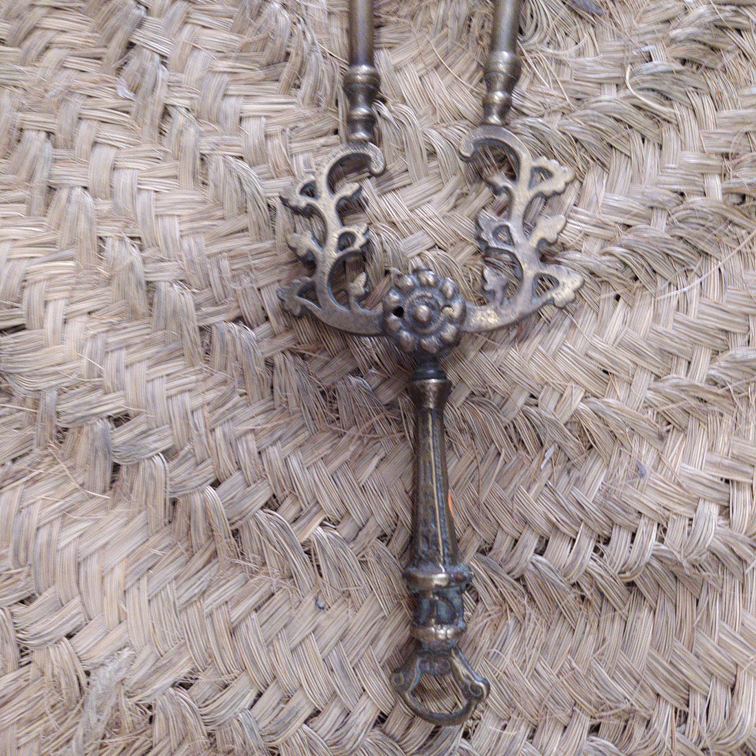 Pinza de chimenea en bronce con diseño ornamental antiguo sobre fondo de mimbre. Decoración elegante para interiores clásicos.