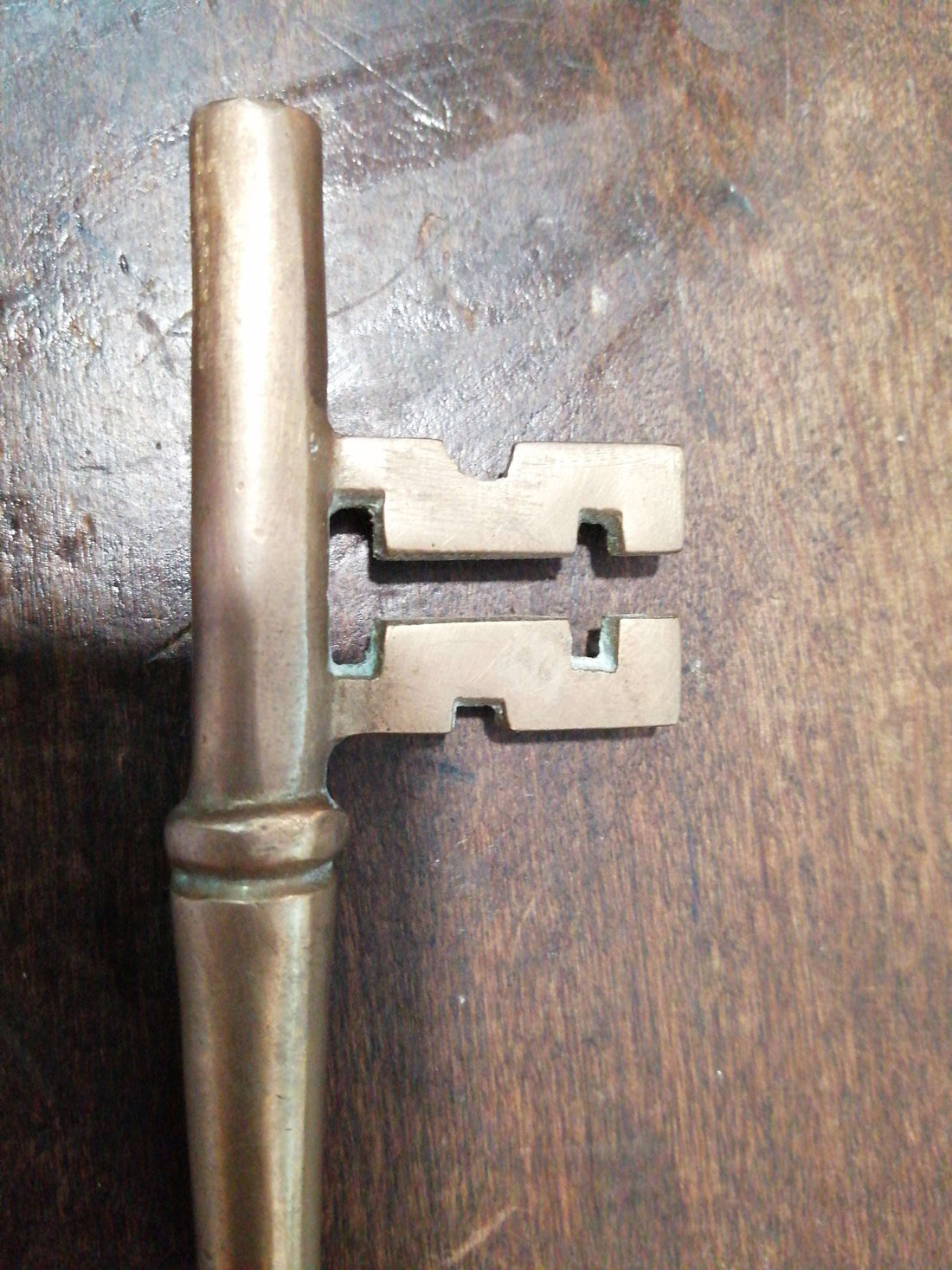 Llave antigua de hierro forjado, siglo XIX, con detalles únicos sobre superficie de madera. Ideal para decoración vintage en hogar o jardín.