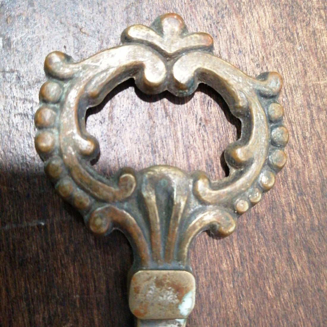 Llave antigua de bronce con detalles ornamentales sobre superficie de madera, ideal para decoración vintage en hogar o colección exclusiva.