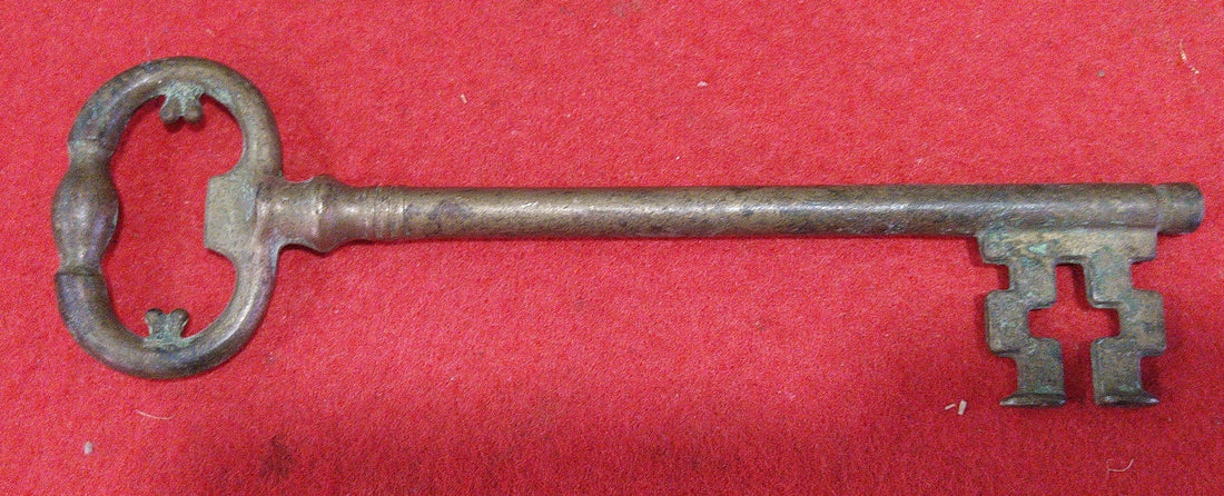 Llave abredor de botellines de metal antiguo estilo vintage sobre fondo rojo, ideal para decoración retro en el hogar o colección temática.