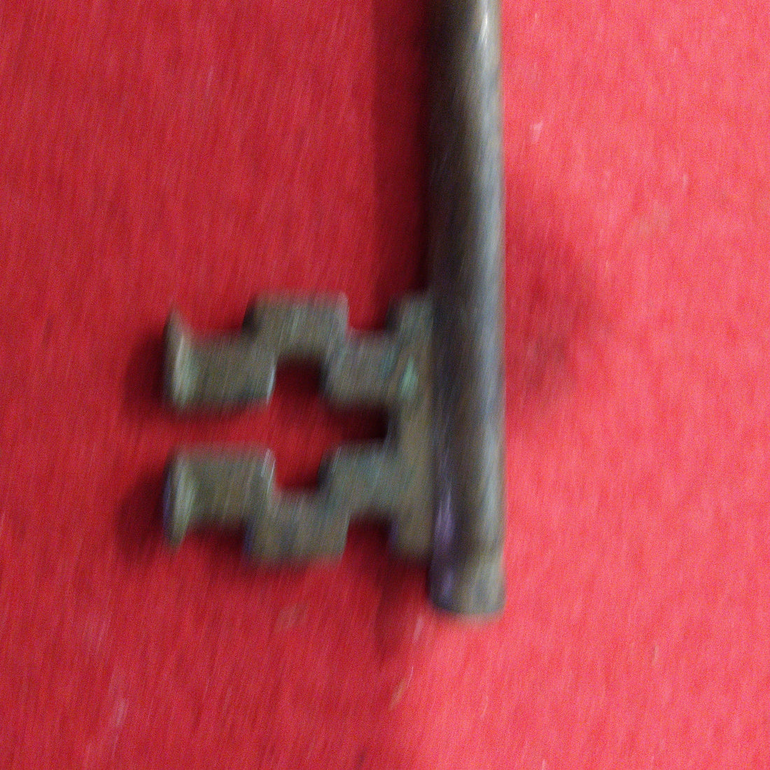 Llave abredor de botellines de metal antiguo estilo vintage sobre fondo rojo, ideal para decoración retro en el hogar o colección temática.