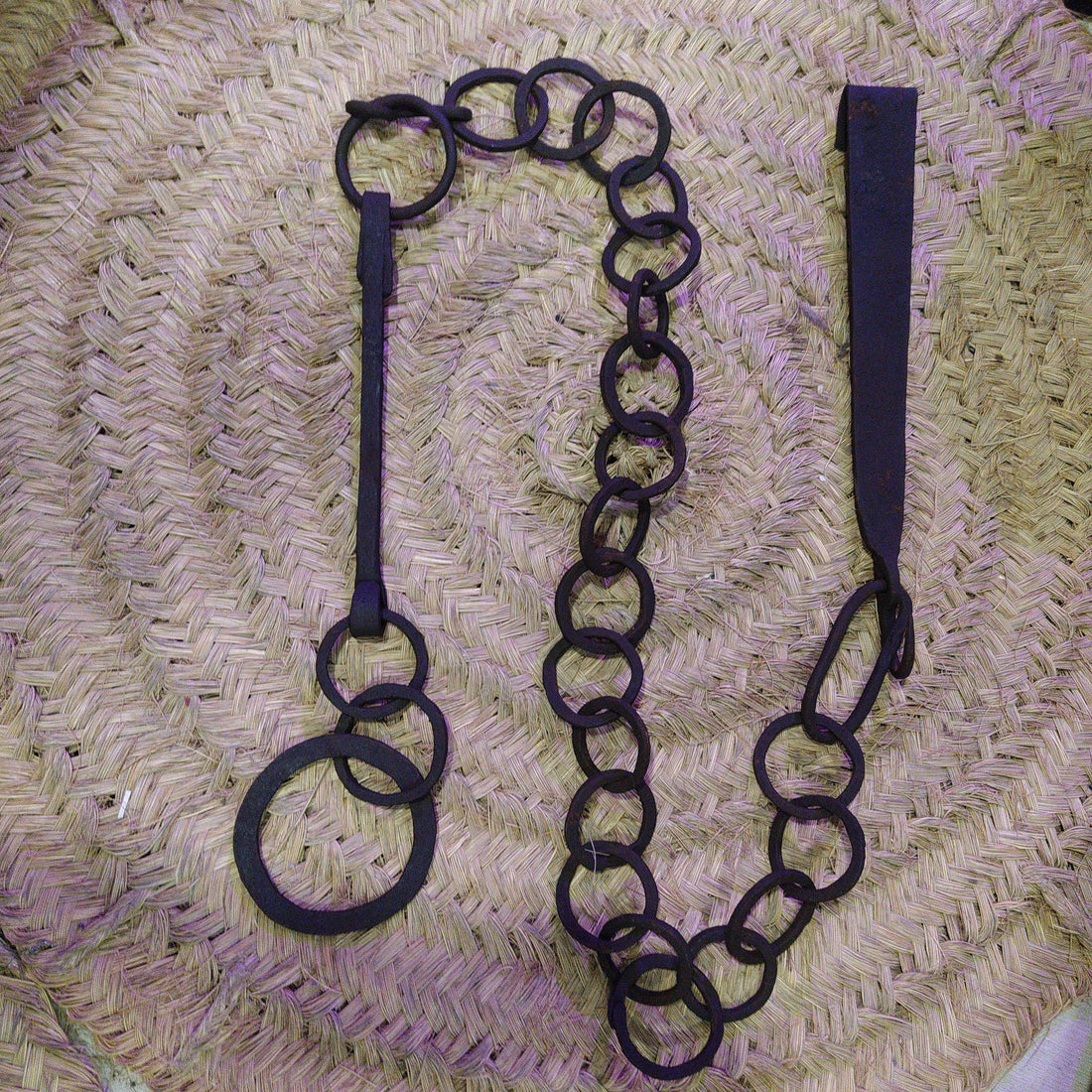 Cadena forjada - LLares de hierro forjado para colgar calderos sobre fondo de mimbre, ideal para decoración rústica de chimeneas.