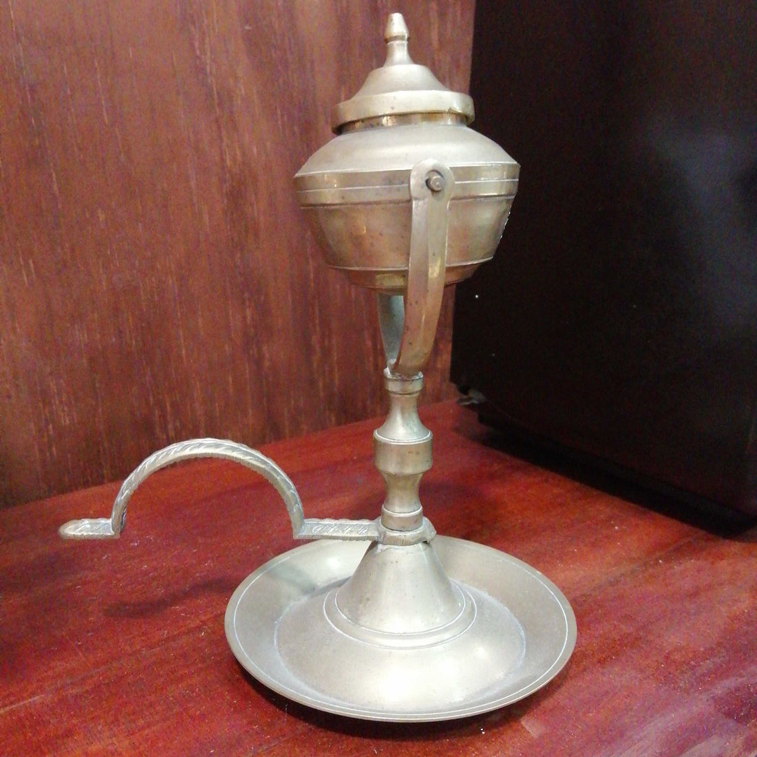 Candil antiguo de aceite en metal basculante de 17 cm sobre mesa de madera. Decoración vintage ideal para coleccionistas y amantes del estilo retro.
