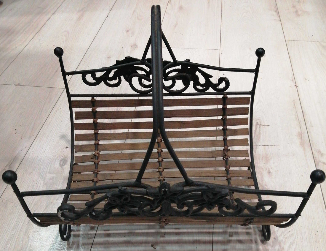 Revistero de forja con detalles ornamentales y base de listones de madera, ideal para decoración rústica en hogar. Calidad excepcional en cada detalle.