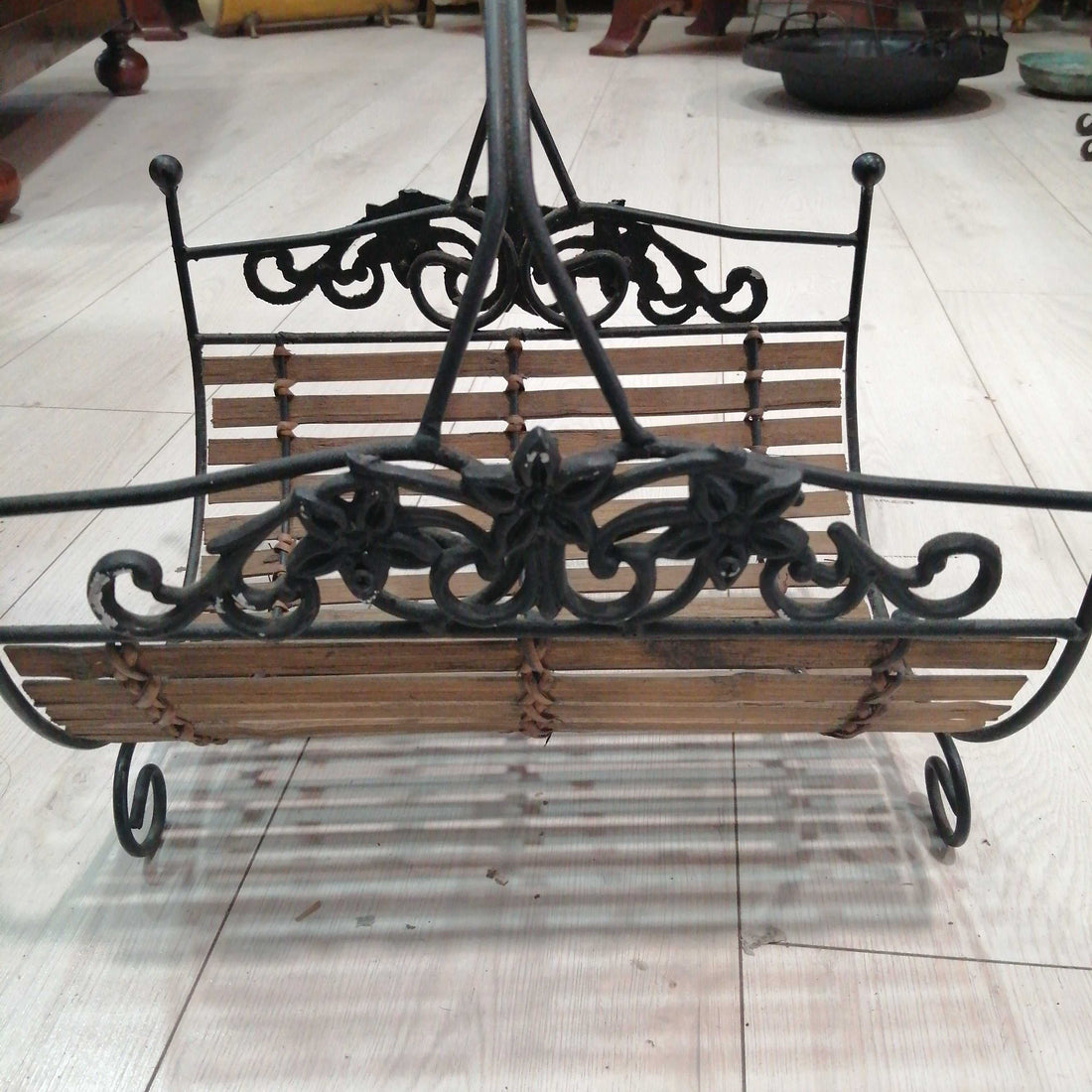 Revistero de forja con detalles ornamentales y base de listones de madera, ideal para decoración rústica en hogar. Calidad excepcional en cada detalle.