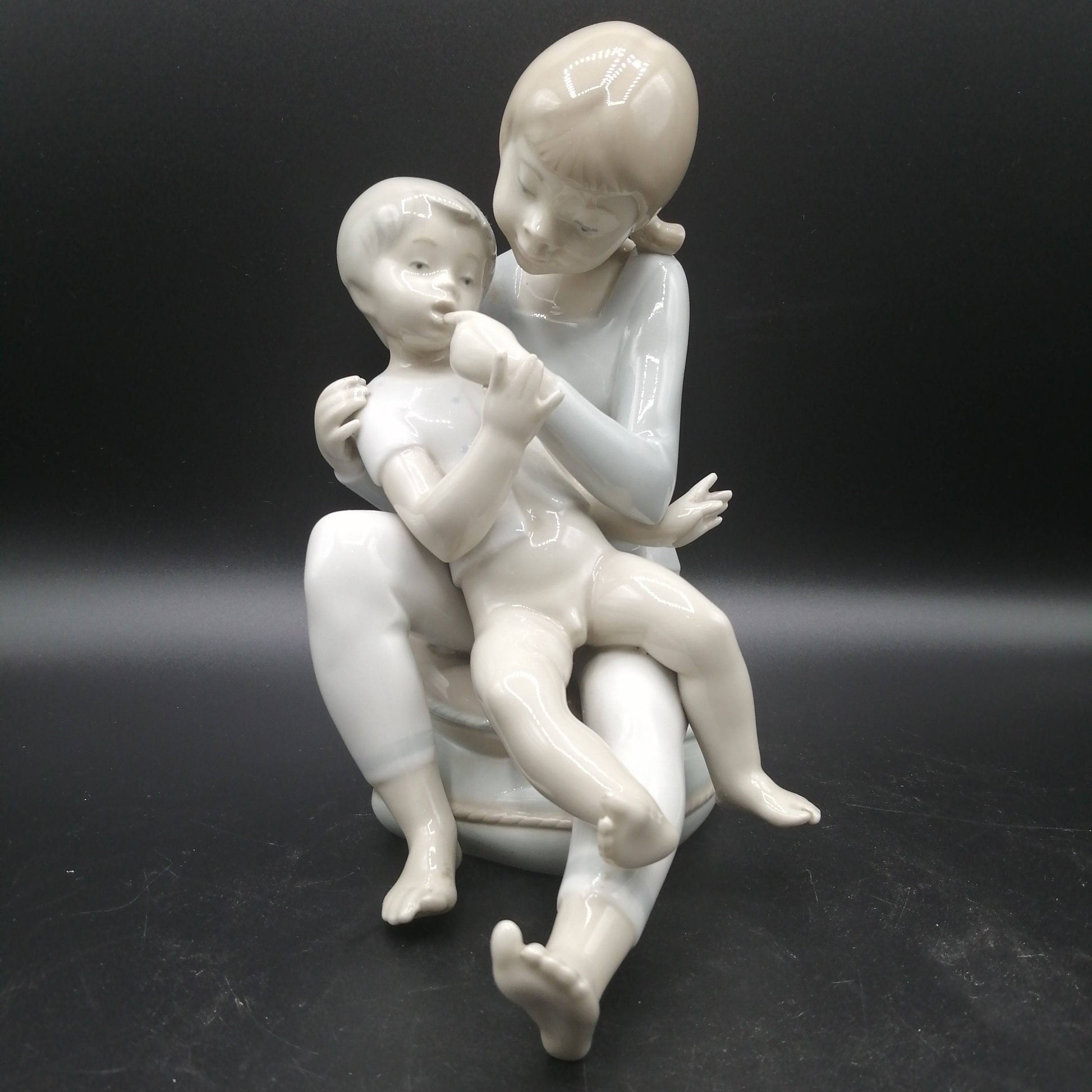 Figura de porcelana niño y niña sentada | Elegancia y calidad con acabado brillante, ideal para decoración vintage en hogar o colección.