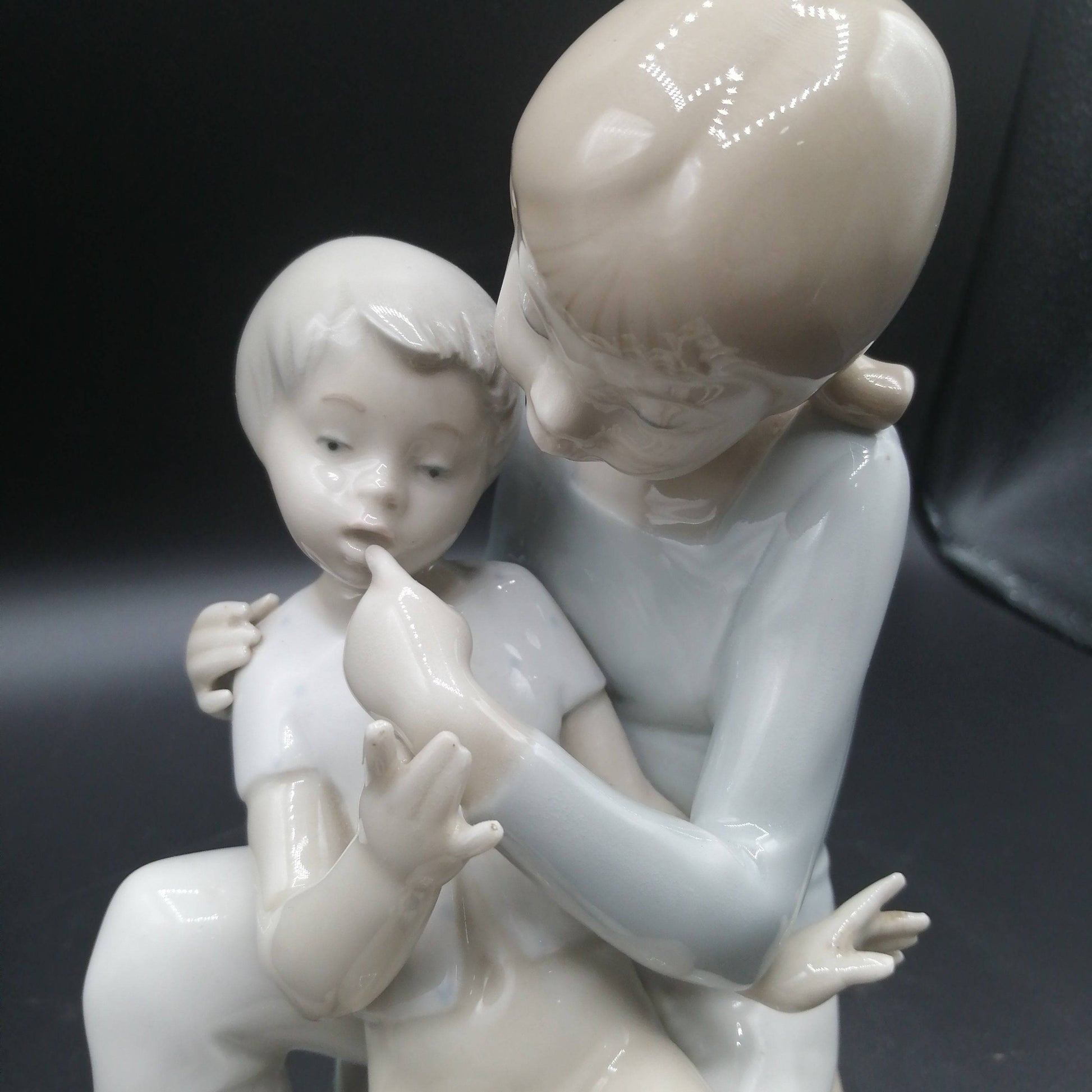 Detalle cercano de figura de porcelana niño y niña sentada | Elegancia y calidad, muestra expresión tierna y acabado fino artesanal.