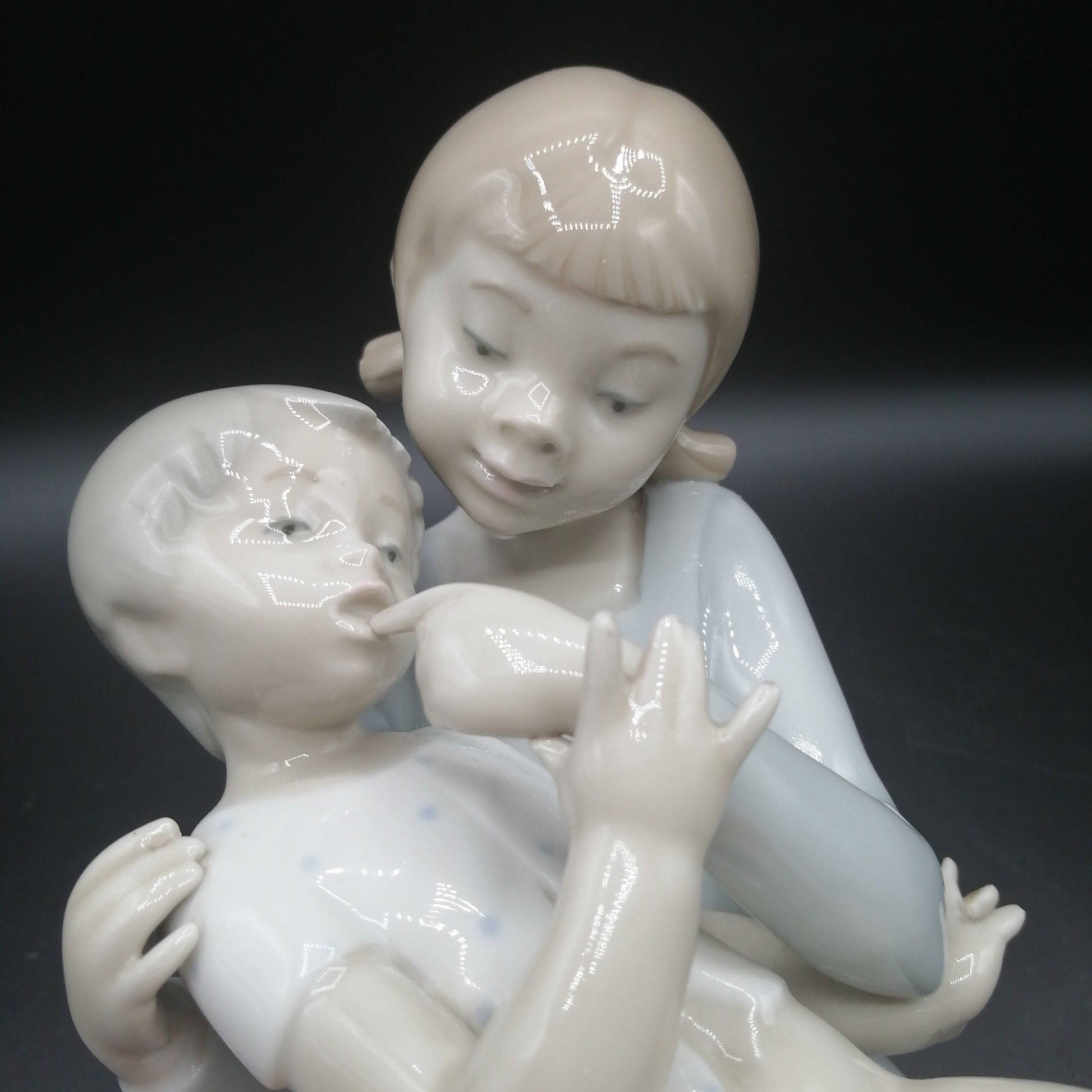 Primer plano de figura de porcelana niño y niña sentada | Elegancia y calidad, destaca el detalle facial y textura esmaltada.