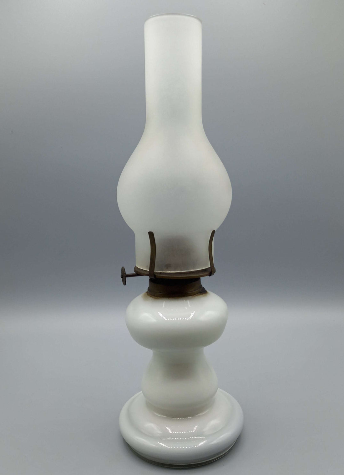 Quinqué de opalina antiguo blanco con base redonda y chimenea alta, ideal para decoración vintage en hogar. Iluminación de época exquisita.