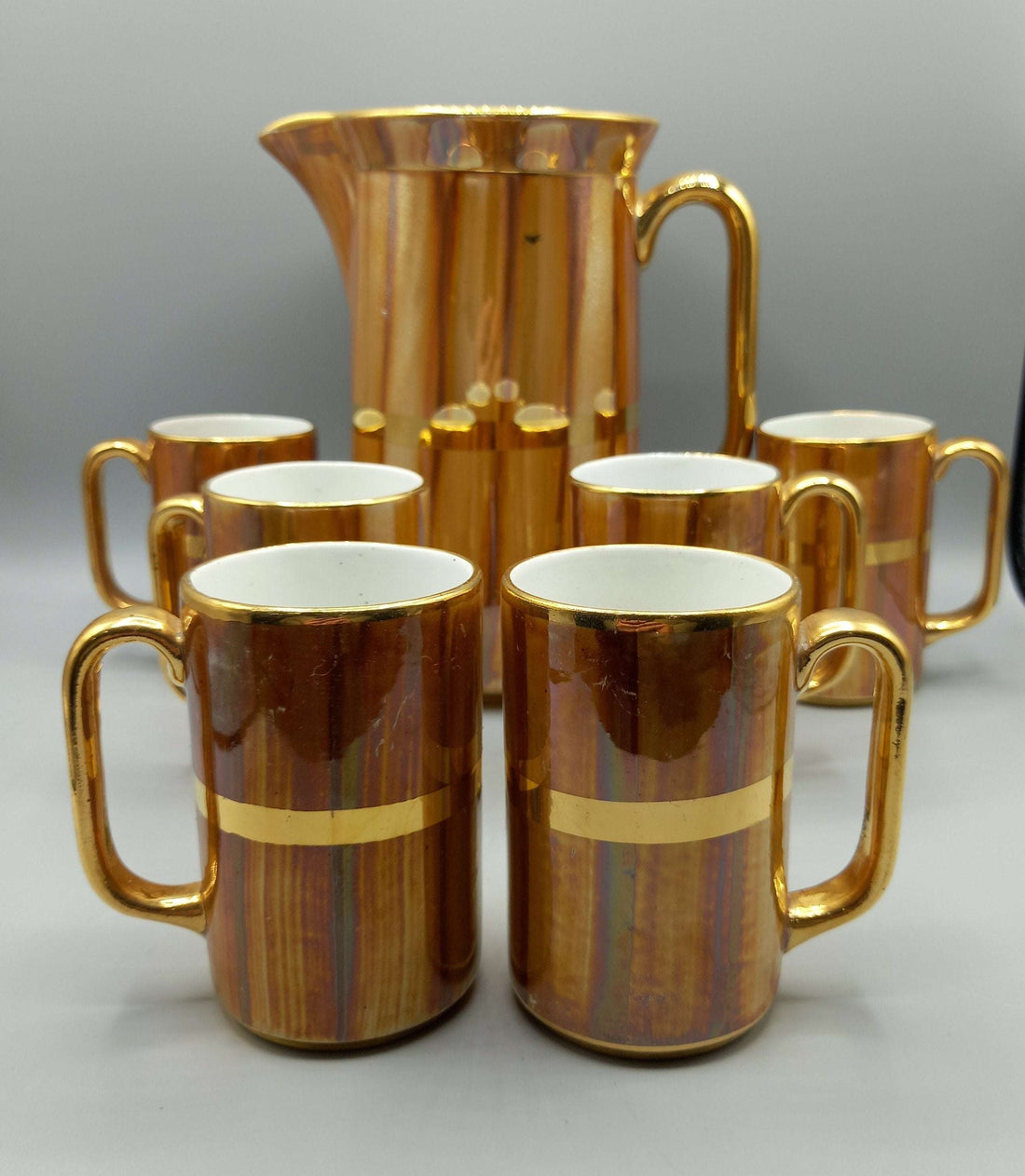 Jarra de porcelana San Claudio con acabado dorado y 6 jarritas a juego, ideal para decoración clásica en el hogar. Diseño vintage para coleccionistas.