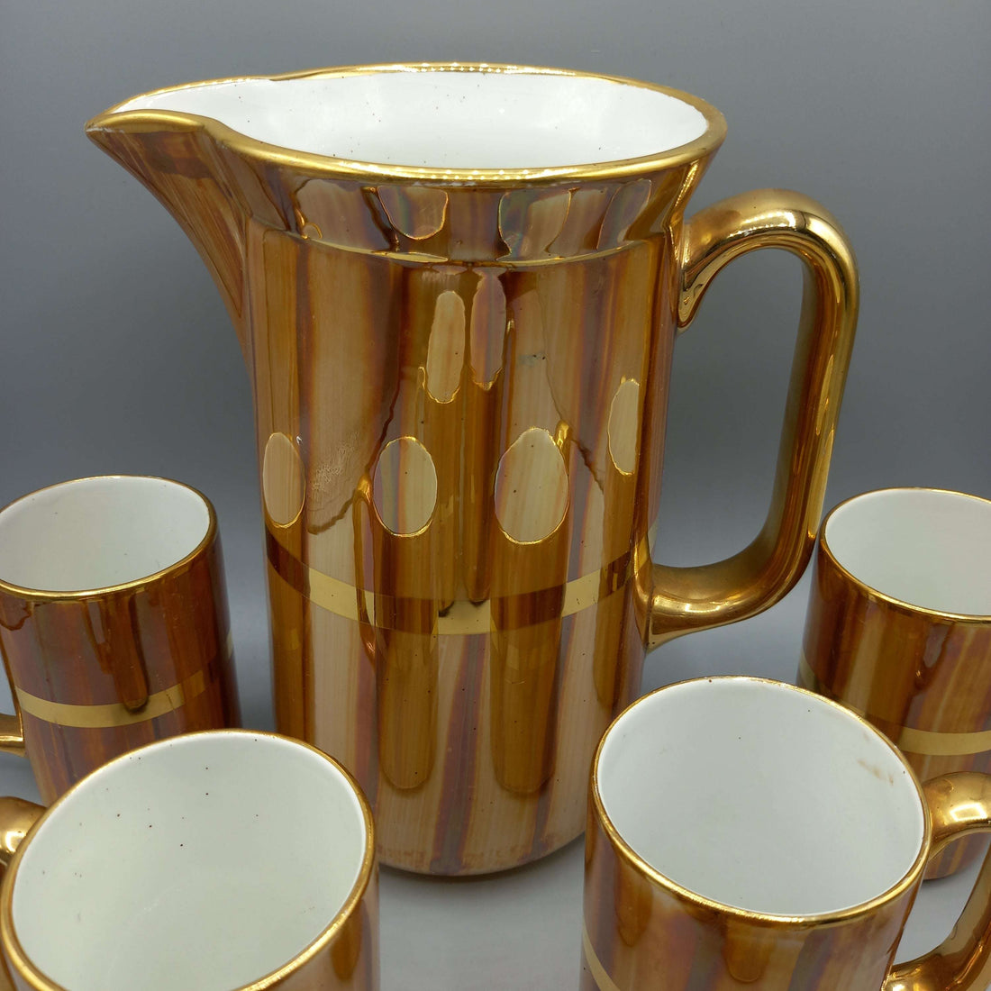 Jarra de porcelana San Claudio con acabado dorado y 6 jarritas a juego, ideal para decoración clásica en el hogar. Diseño vintage para coleccionistas.