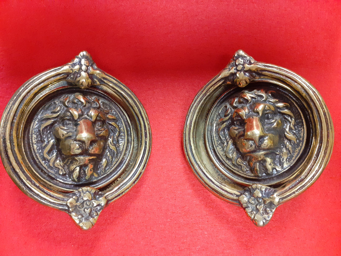 Aldabas antiguas en forma de argolla y cabeza de león en bronce sobre fondo rojo. Decoración clásica ideal para puertas elegantes de jardín o casa.