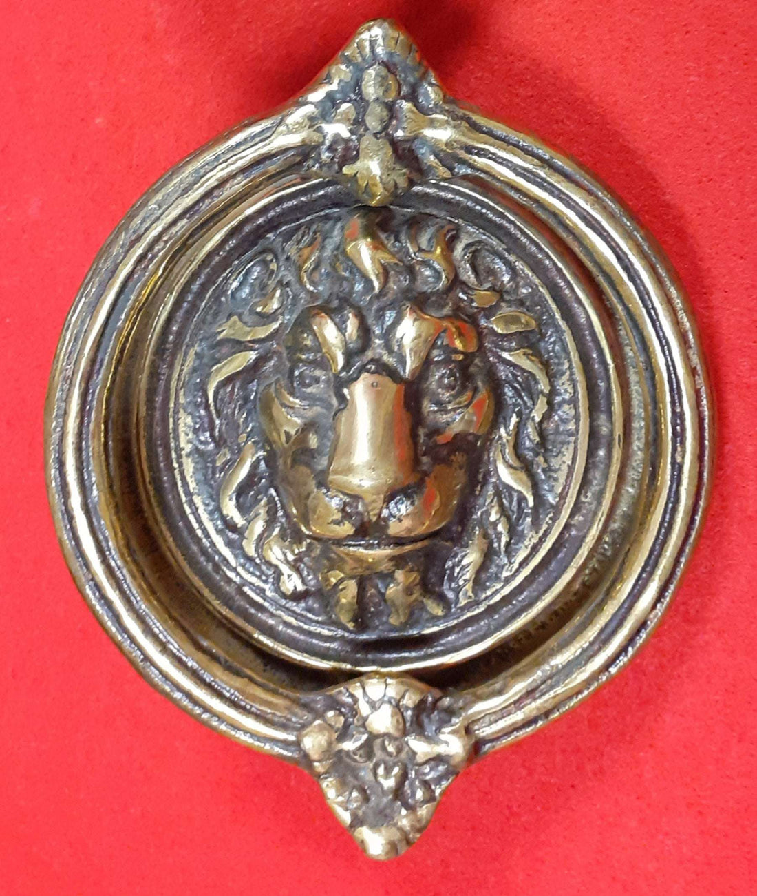 Aldabas antiguas en forma de argolla y cabeza de león en bronce sobre fondo rojo. Decoración clásica ideal para puertas elegantes de jardín o casa.