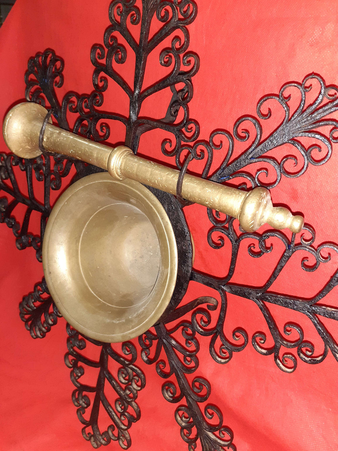Mortero con filigranas antiguas de metal sobre fondo rojo, ideal para decoración de pared única en estilo vintage. Pieza exclusiva de almirez colgante.