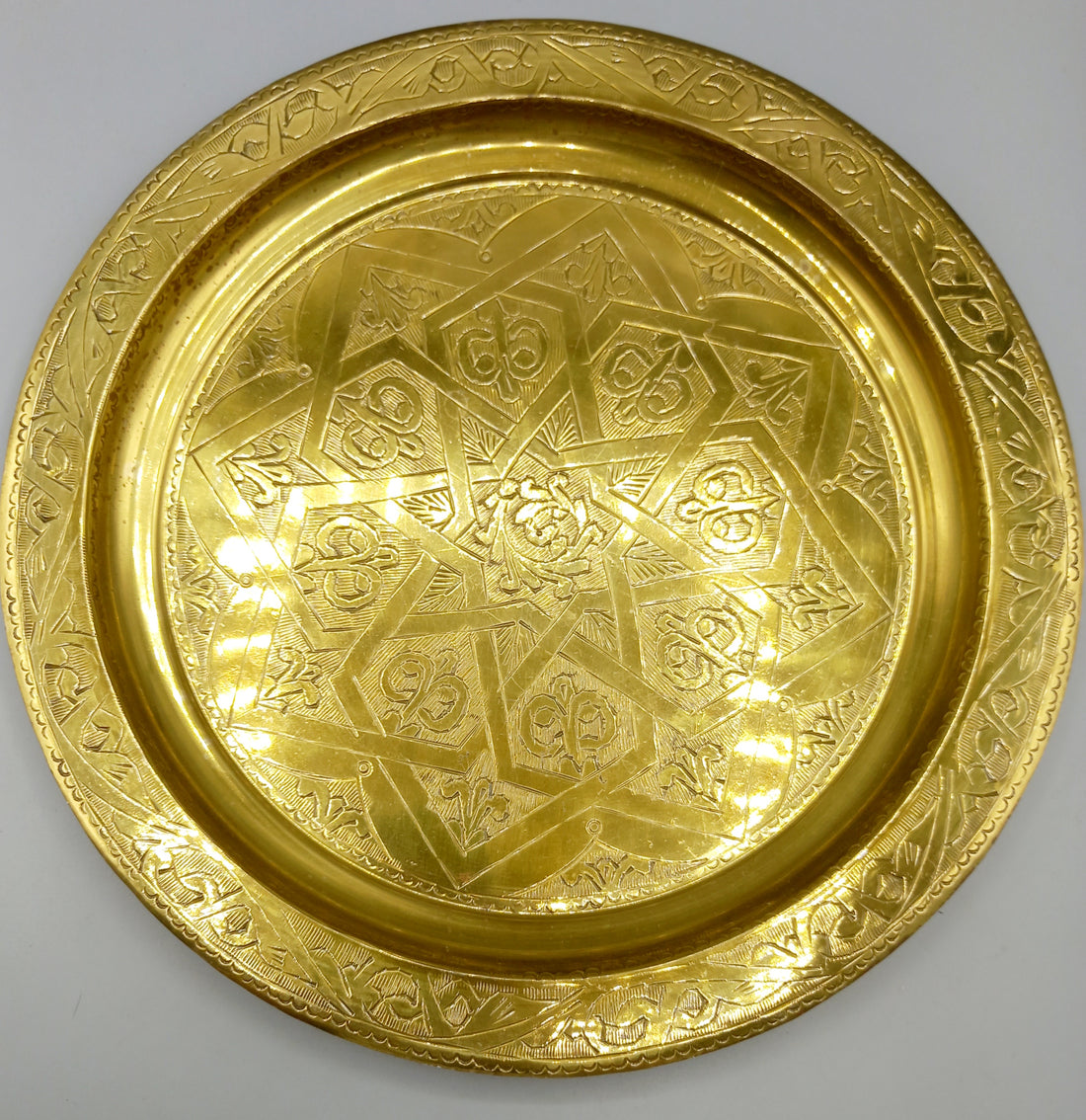 Plato repujado de metal dorado con diseño geométrico exclusivo, ideal para decoración elegante en el hogar. Excelente calidad artesanal.