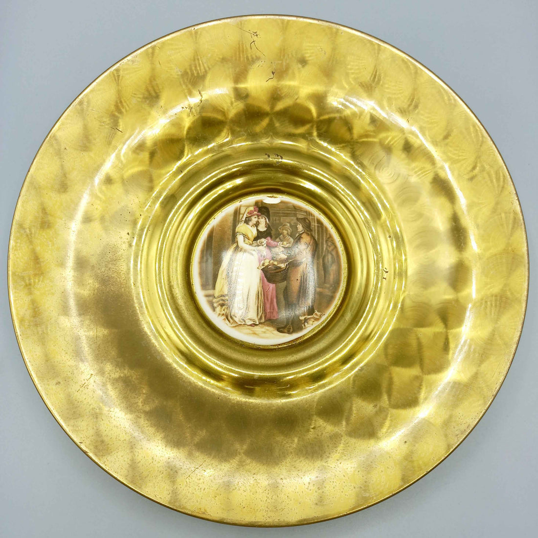 Plato de metal esmaltado, elegante y de excelente calidad con acabado dorado texturizado y escena clásica pintada al centro, ideal para decoración.