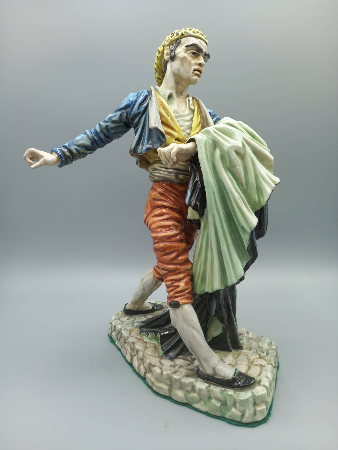 Figura Bandolero Porcelana - Algora Torero en pose dinámica, vestimenta goyesca con chaqueta azul y pantalón rojo, sobre base de piedra.