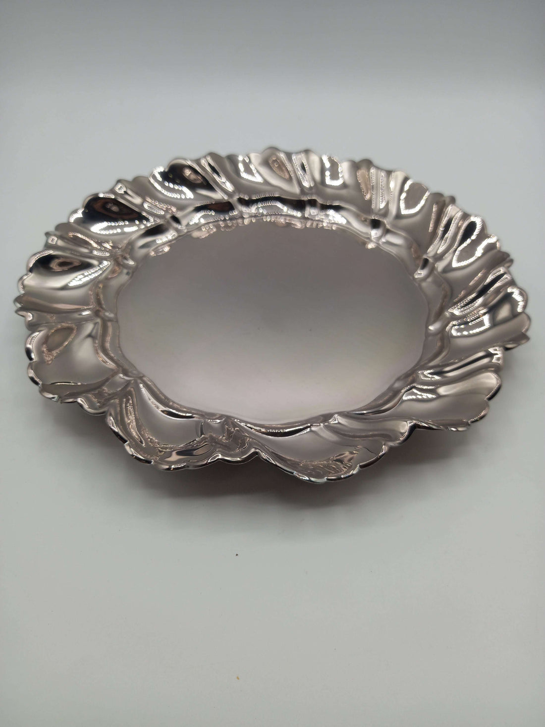 Elegante plato de metal plateado con borde ondulado, ideal para decoración refinada en el hogar o eventos especiales.