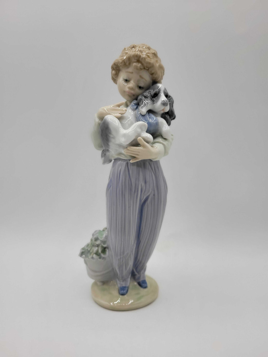 Figura Lladró 'Perrito Convaleciente' de 1989 en porcelana, muestra a un niño con pijama a rayas sosteniendo un perrito enfermo. Edición limitada ideal para decoración de interiores.
