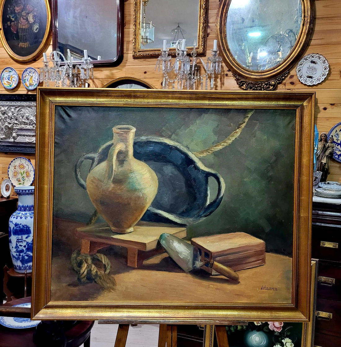 Óleo Bodegón con Marco Dorado Antiguo – Firma Lázaro exhibido en tienda de decoración, con jarrón, paleta y libro sobre fondo clásico.