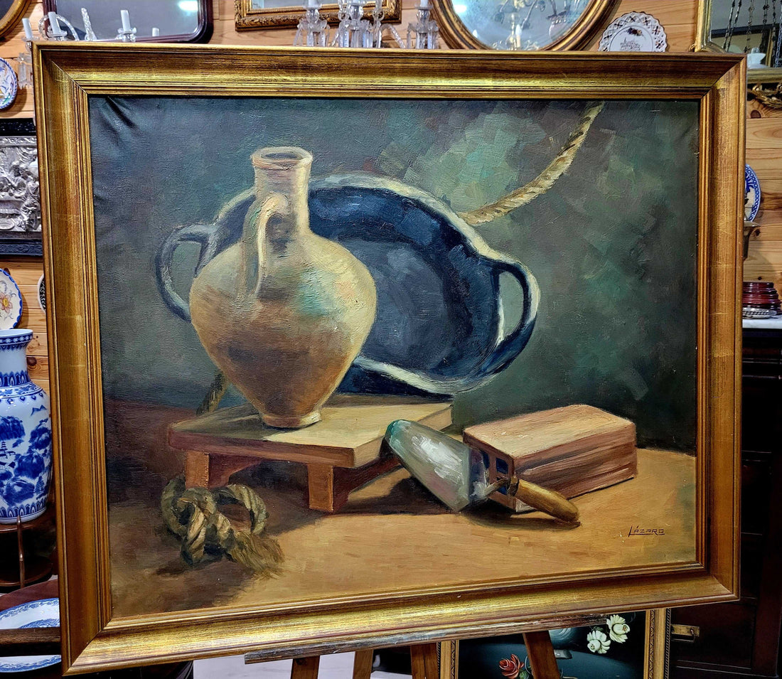 Óleo Bodegón con Marco Dorado Antiguo – Firma Lázaro exhibido en tienda de decoración, con jarrón, paleta y libro sobre fondo clásico.
