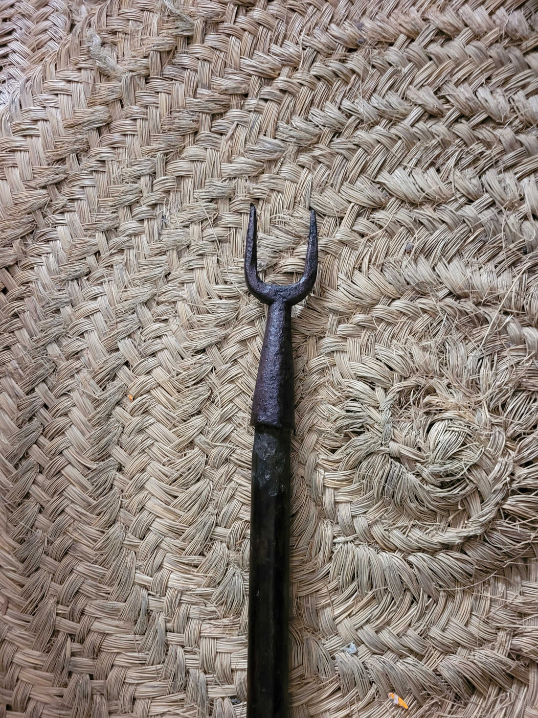 Horquilla antigua de hierro con largo palo de madera sobre suelo de piedra.