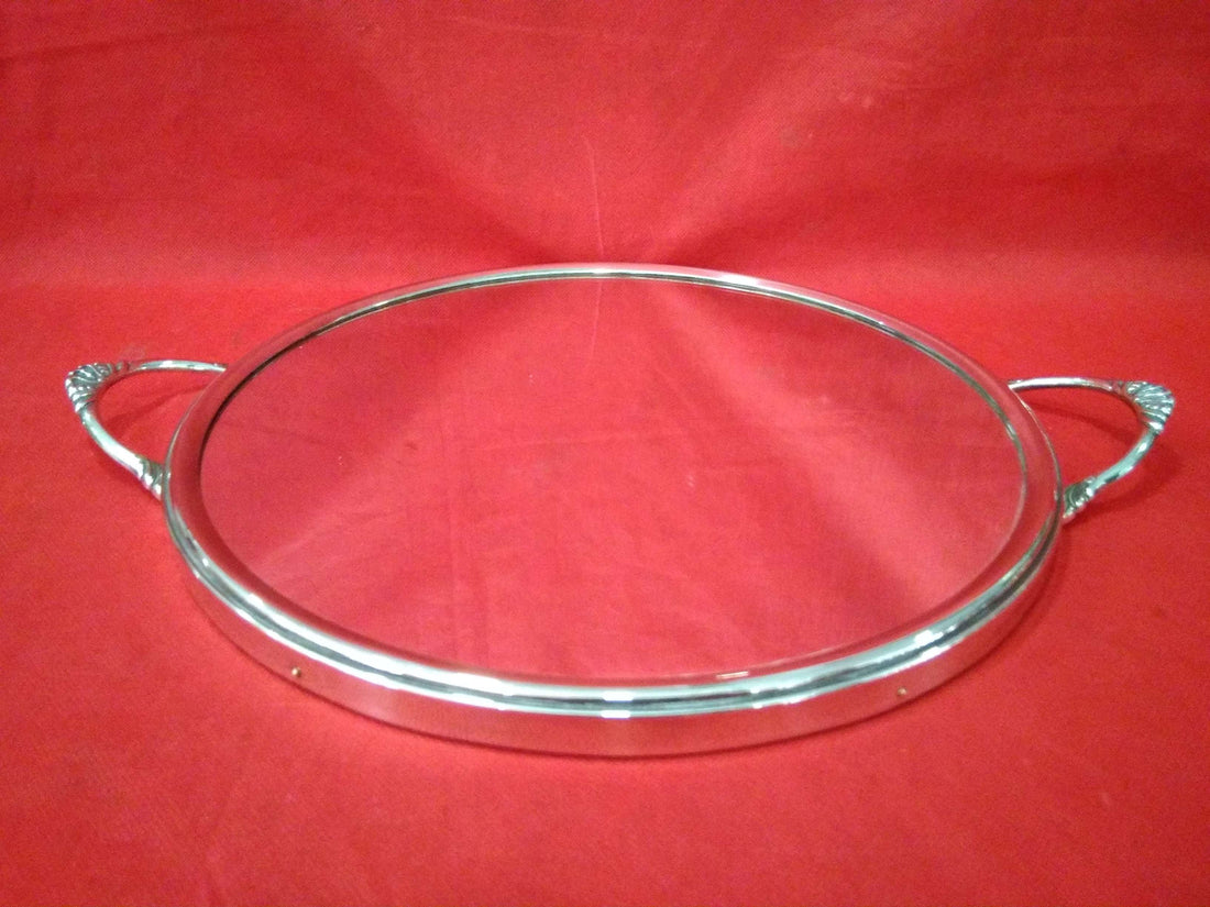 Bandeja redondeada de metal plateado espejada con asas decorativas sobre fondo rojo. Diseño elegante ideal para decoración o servir.