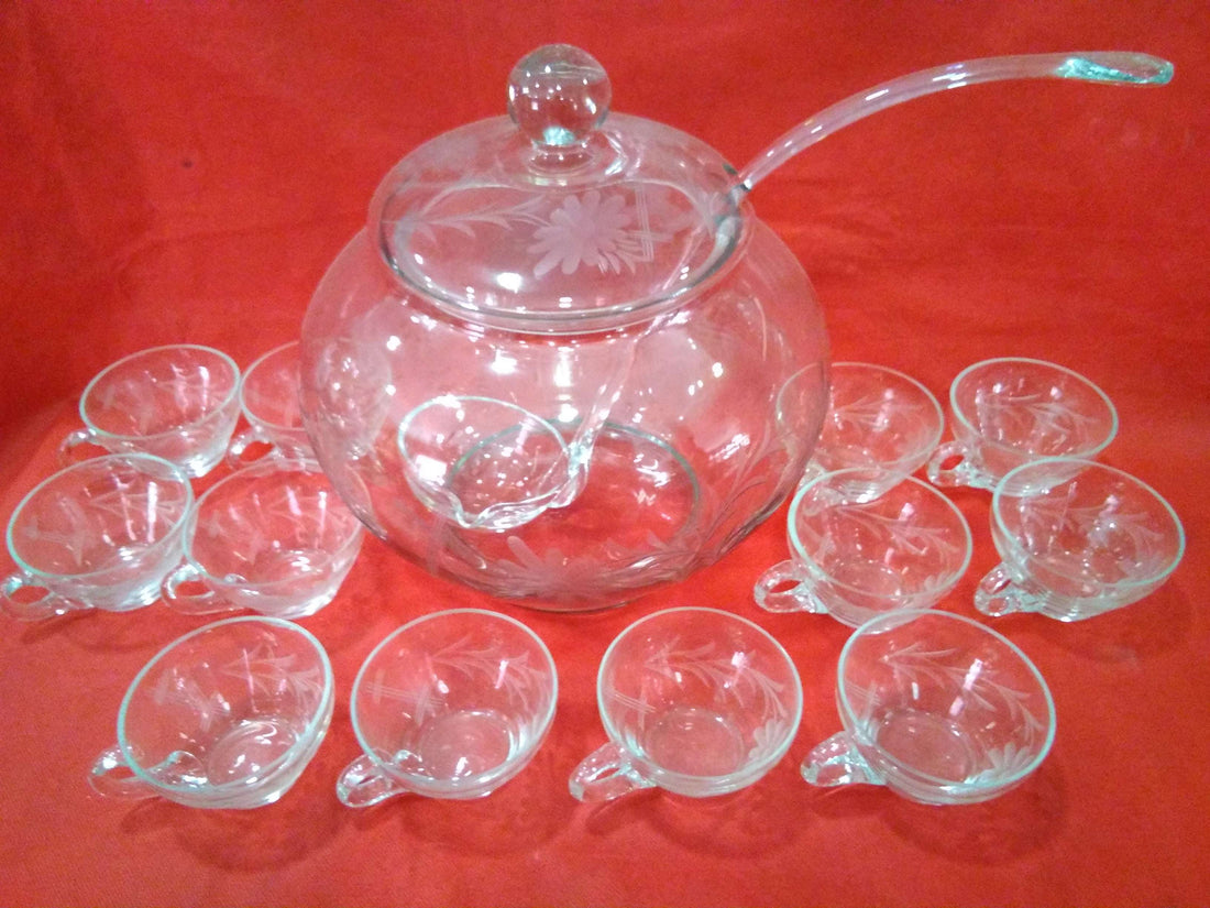 Ponchera de cristal grabado con 12 tazas sobre fondo rojo, ideal para decoración elegante en eventos especiales. Diseño antiguo y calidad excepcional.