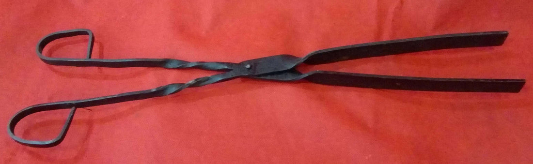 Pinza para brasero en hierro forjado sobre fondo rojo, ideal para decoración rústica y colecciones vintage de herramientas antiguas.