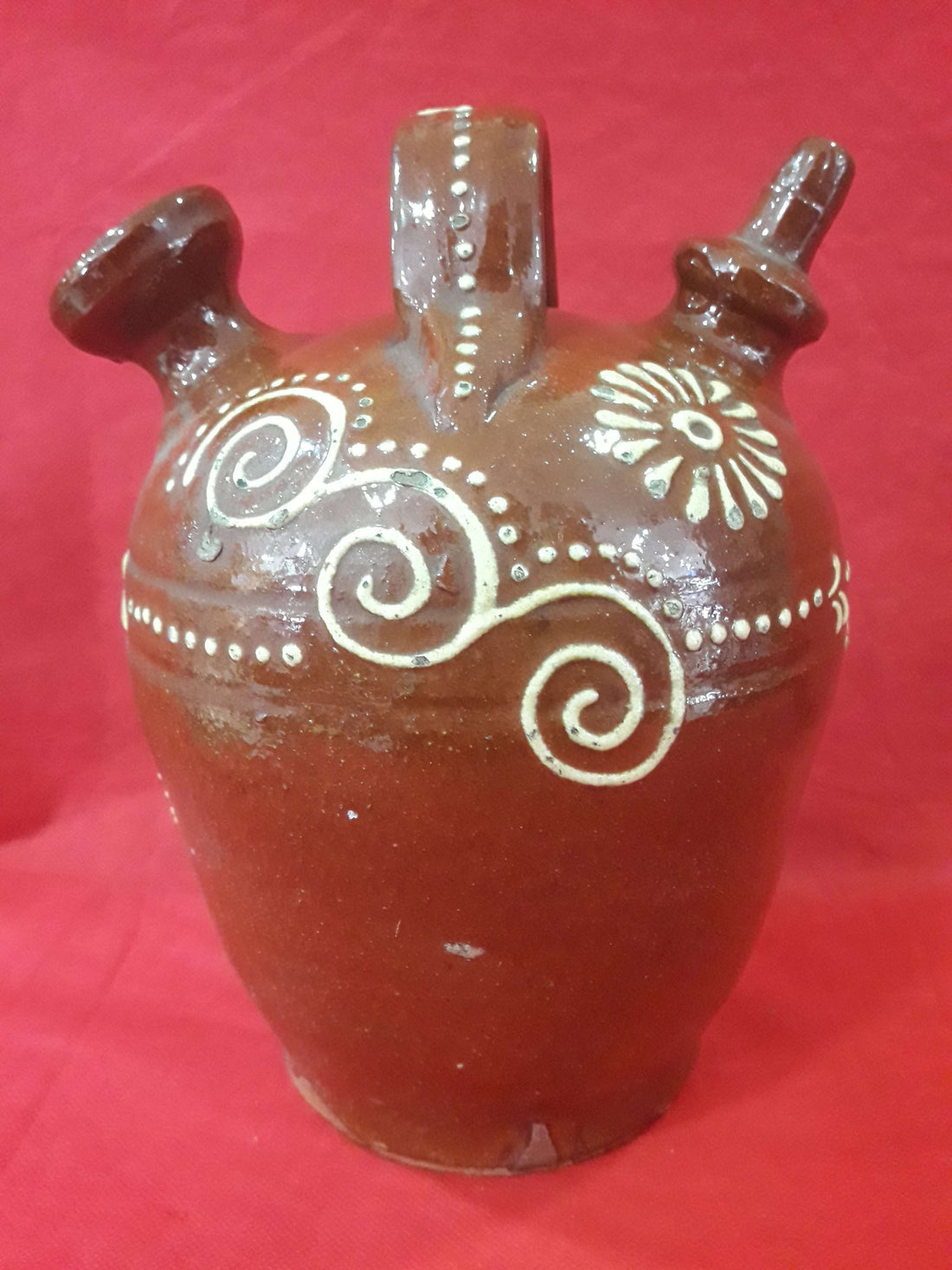 Botijo de cerámica esmaltado pintado a mano con diseño floral y espirales en blanco sobre fondo marrón. Decoración artesanal de excelente calidad.