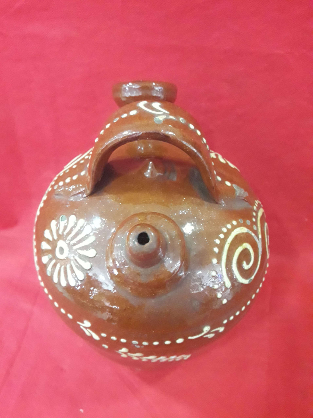 Botijo de cerámica esmaltado pintado a mano con diseño floral y espirales en blanco sobre fondo marrón. Decoración artesanal de excelente calidad.