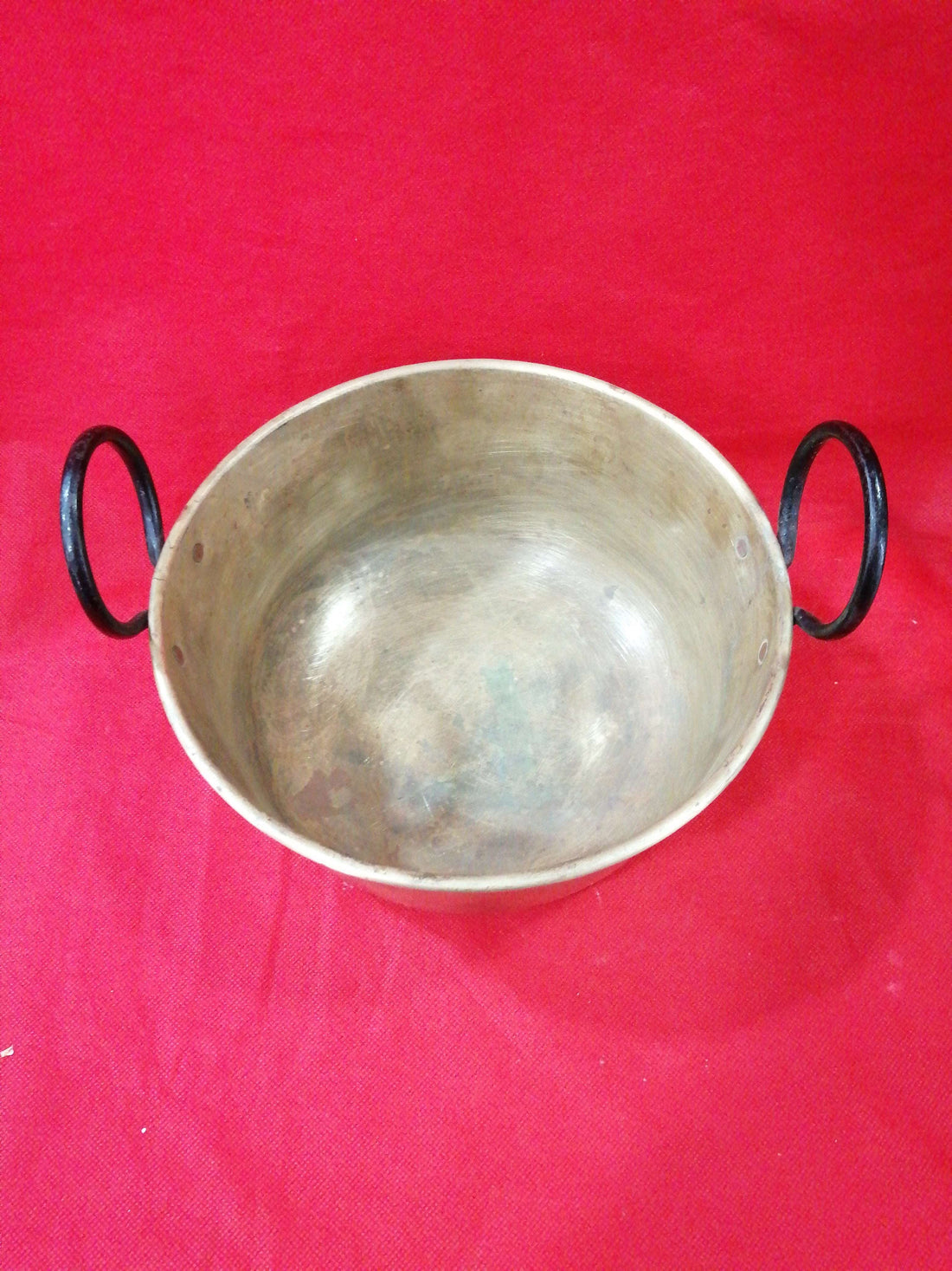 Caldero de metal con asas de hierro en fondo rojo, ideal para decoración vintage en hogar o jardín. Excelente calidad y estado de conservación.