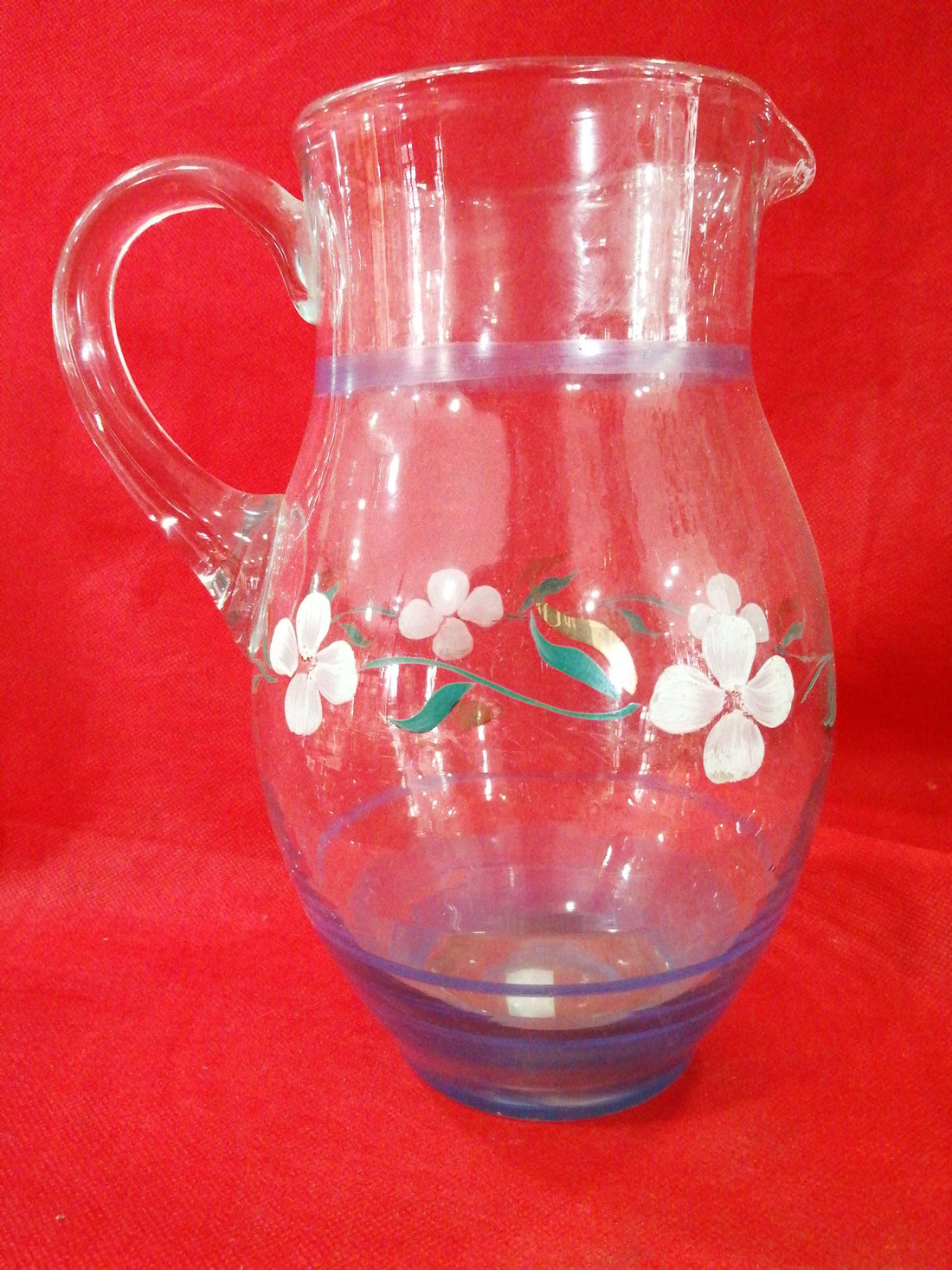 Jarra de cristal antigua decorada a mano con flores blancas y hojas verdes sobre fondo rojo. Ideal para decoración vintage en el hogar.