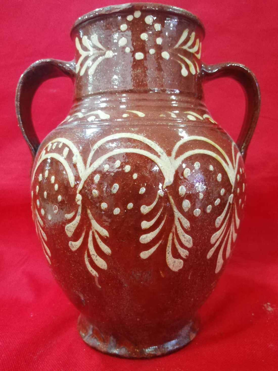 Ánfora antigua de barro pintada a mano con diseño floral en blanco sobre fondo marrón, ideal para decoración rústica y coleccionismo exclusivo.