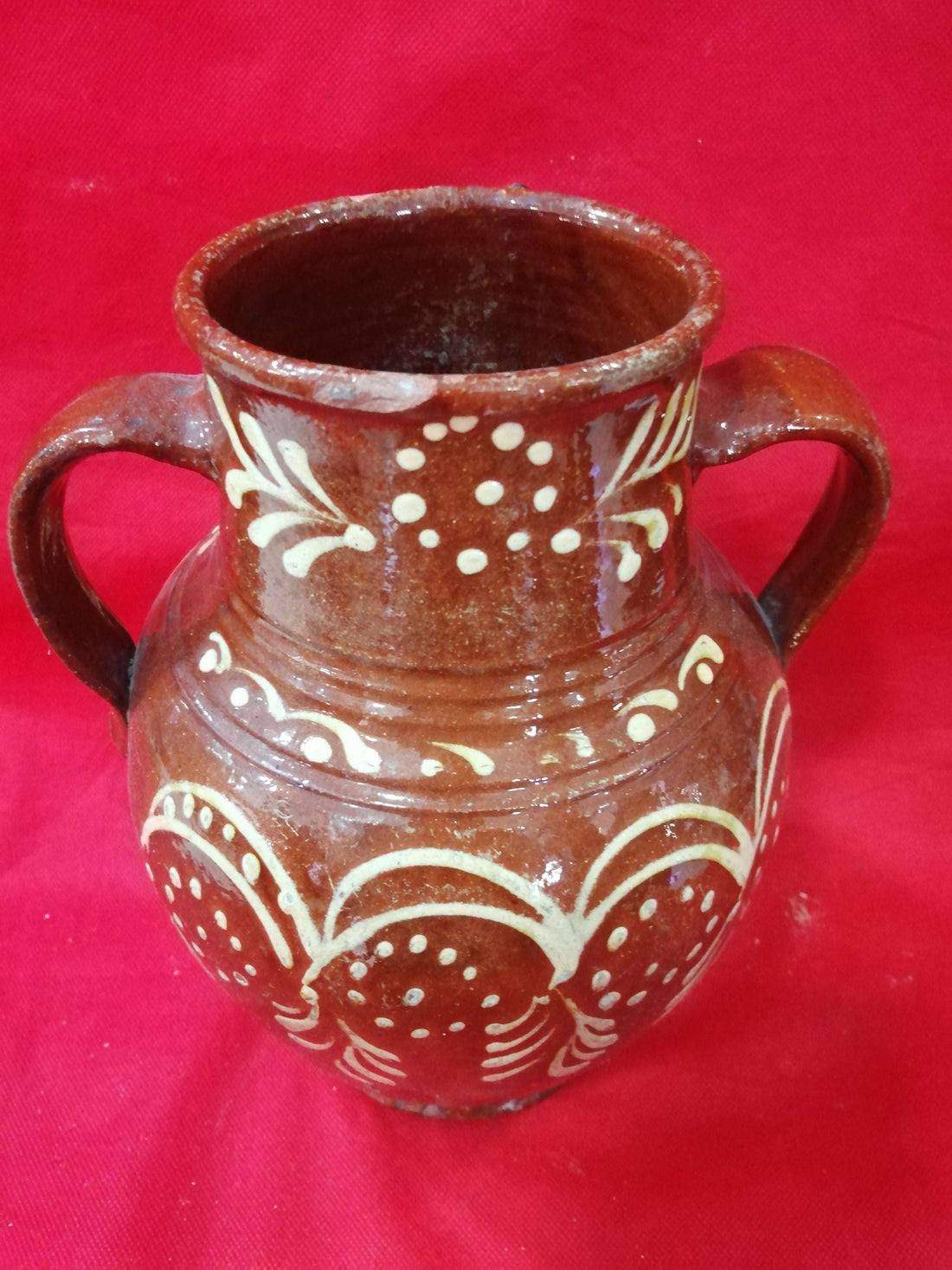 Ánfora antigua de barro pintada a mano con diseño floral en blanco sobre fondo marrón, ideal para decoración rústica y coleccionismo exclusivo.