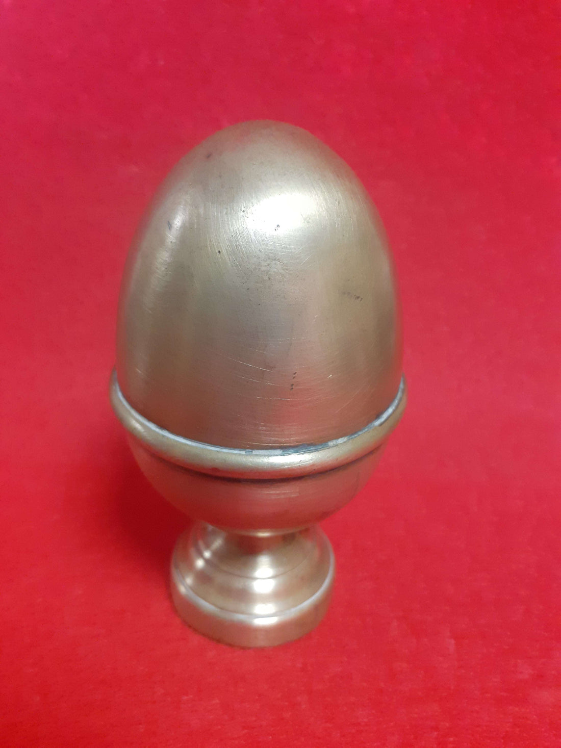 Remate decorativo en forma de piña de metal antiguo sobre fondo rojo, ideal para balcones y escaleras clásicas. Estilo vintage para decoración.