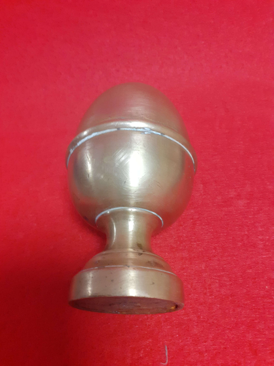 Remate decorativo en forma de piña de metal antiguo sobre fondo rojo, ideal para balcones y escaleras clásicas. Estilo vintage para decoración.