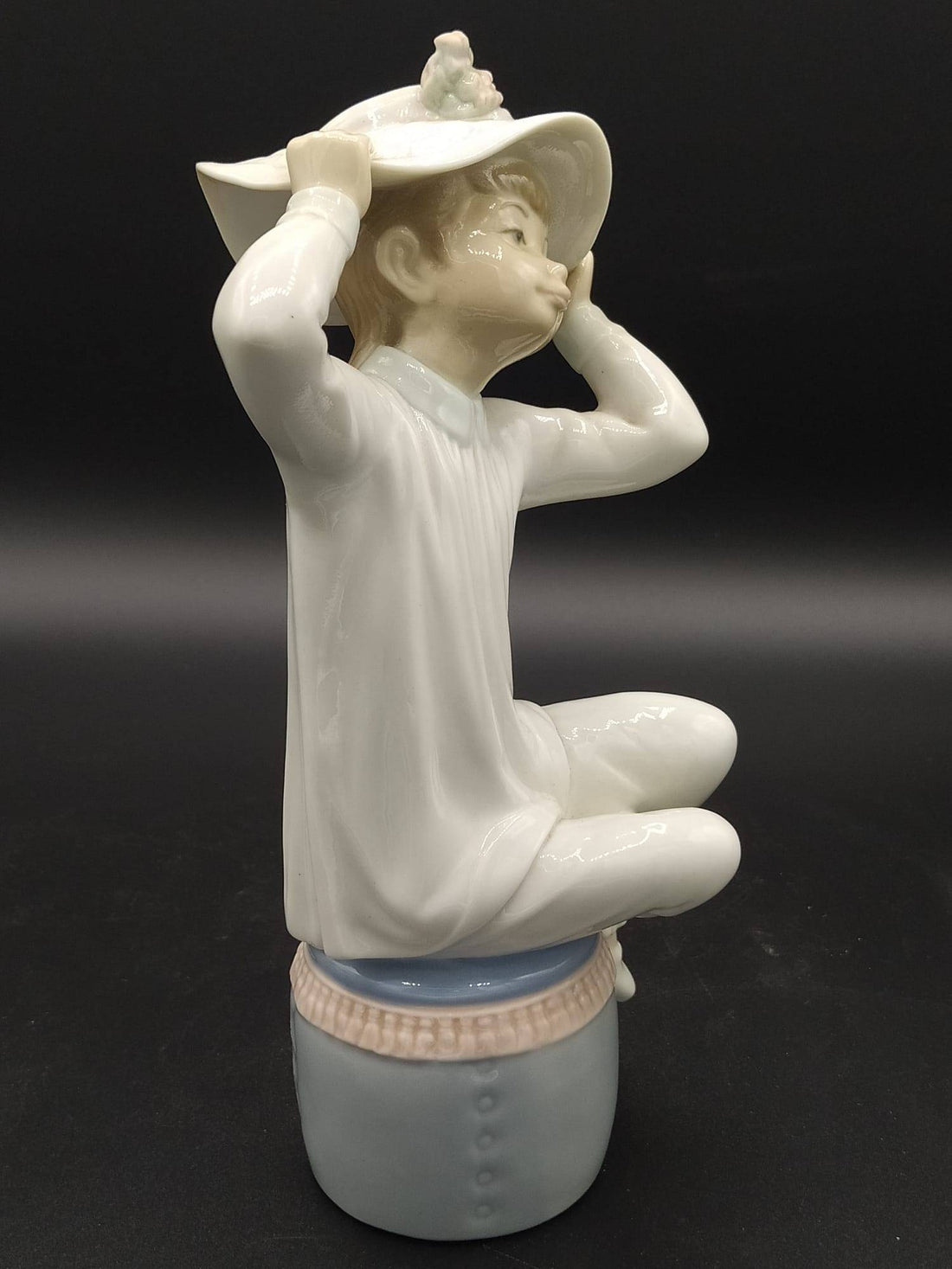 Figura de porcelana Lladró 'Chica con gorro' sentada sobre un tambor azul, con vestido blanco y sombrero decorado, ideal para decoración elegante.