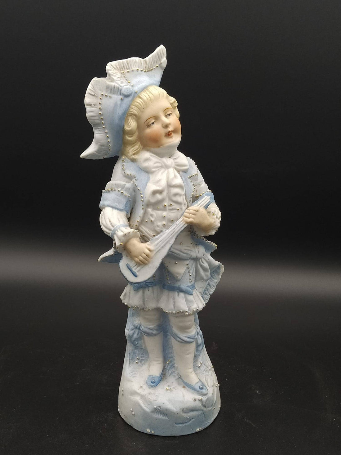 Figura de porcelana antigua de galleta, niño tocando cuerda, excelente, con vestimenta azul estilo rococó sobre fondo negro.
