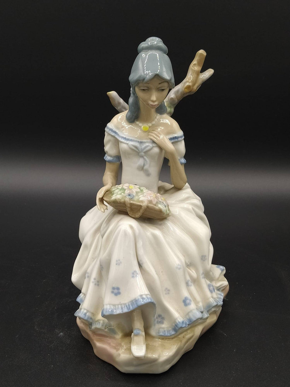 Figura de porcelana Mujer con Flores de Casades sentada con vestido blanco y detalles florales, ideal para decoración elegante de interiores.