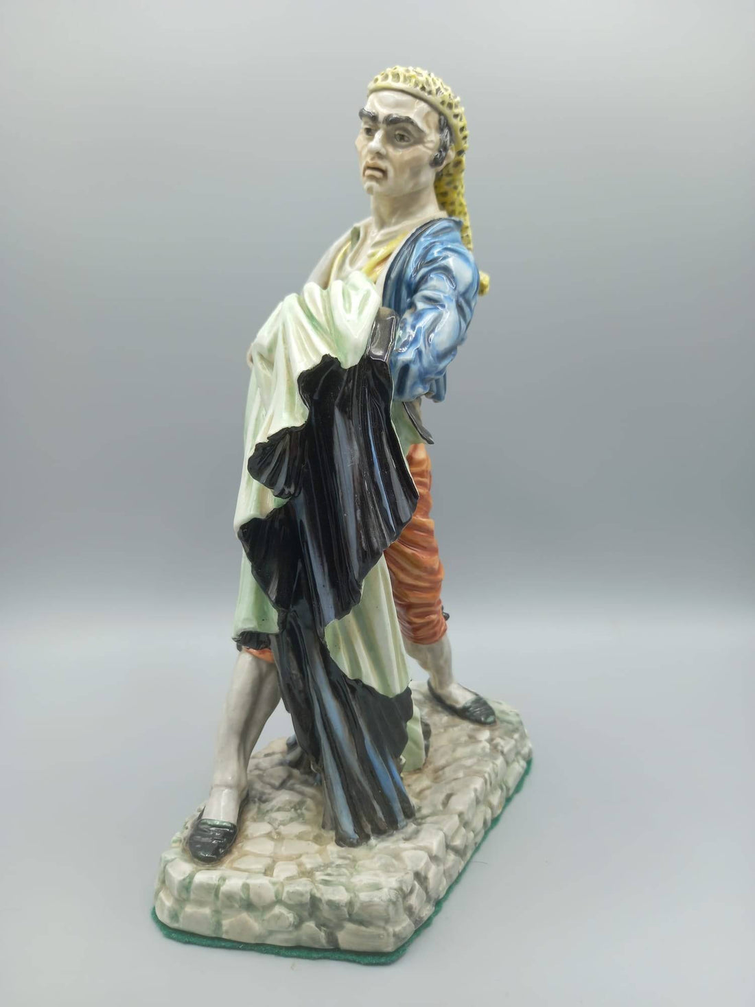 Figura Bandolero Porcelana - Algora Torero en pose dinámica, vestimenta goyesca con chaqueta azul y pantalón rojo, sobre base de piedra.