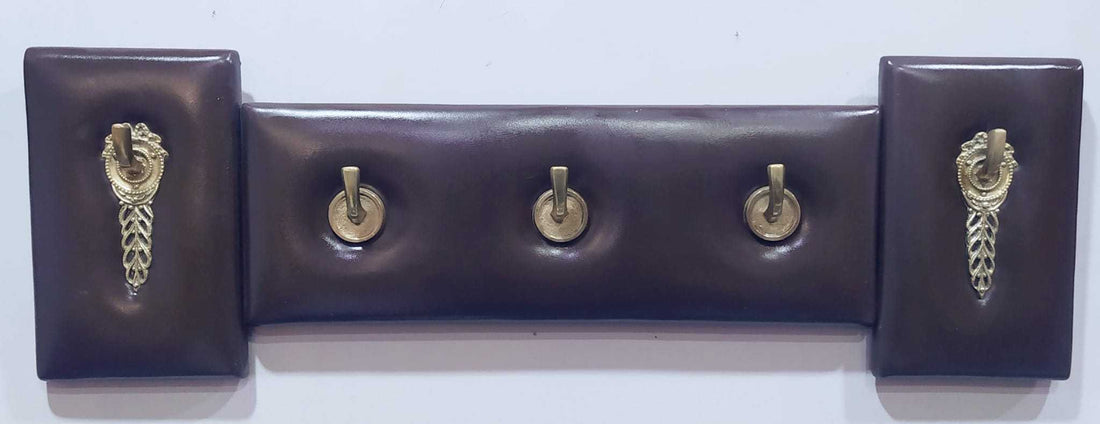 Perchero en metal y cuero de estilo elegante y exclusivo con cinco ganchos dorados sobre base acolchada marrón. Ideal para decoración vintage y moderna.