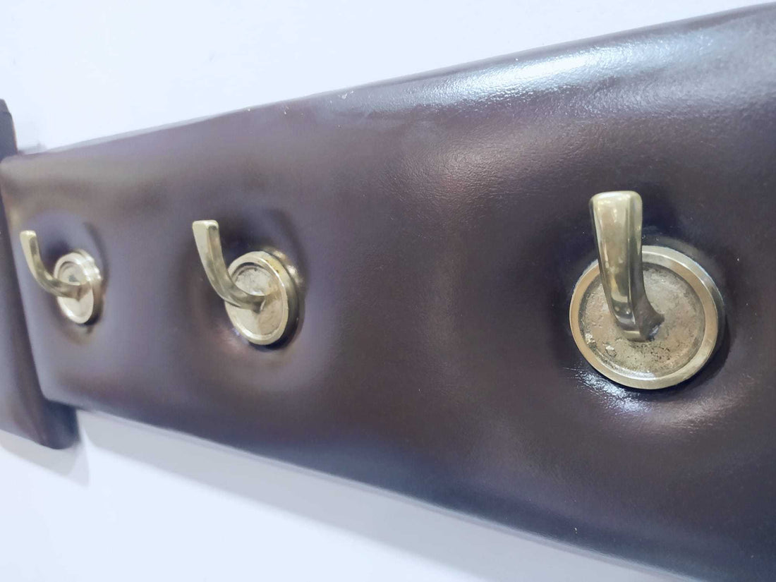 Perchero en metal y cuero de estilo elegante y exclusivo con cinco ganchos dorados sobre base acolchada marrón. Ideal para decoración vintage y moderna.