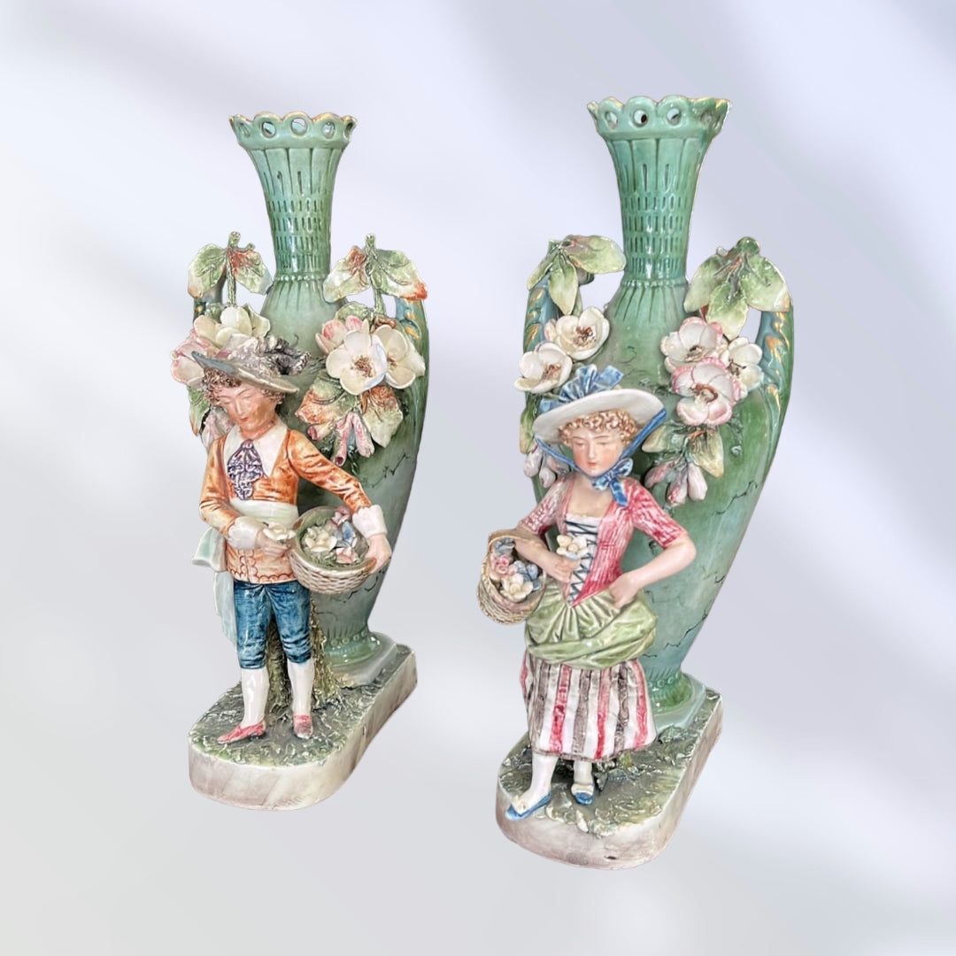 Pareja de floreros artísticos de porcelana pintados a mano, con figuras de campesinos y decoración floral inspirada en el siglo XIX.